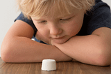 Cute child looks at single marshmallow on table.