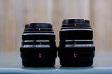 Fujifilm XF 35mm F2 R WR and 23mm F2 R WR lenses side by side on a table, showcasing their compact design and aperture settings.