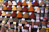A lovely display of spices in a market, where various spices are in a conical pile along with their prices.