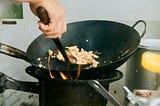 A person cooking food in a wok on a stove.