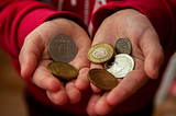 A child’s hands in a red sweater holding 6 coins