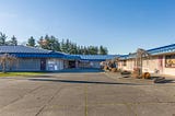 Frontal view of a one story school made of brick and cinder block with a metal roof on a clear day