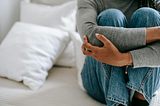 Person Sitting On Bed With Crawled Kneel And Arms Rapped Around Them