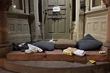 A doorway with food packaging and cushions for sleeping