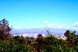 A mountain vista with blue sky, a few distant clouds and greenery.