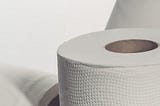 Close up of a paper product, either a roll of toilet paper or paper towels. The roll is stark against a plain white background.