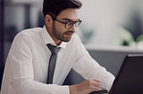 A young CEO is sitting behind his desk, working on his laptop.