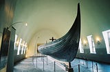 A viking ship is displayed in a long arched ceiling room.