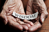 Wrinkled hands holding a paper that says ‘wisdom’