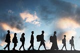 a group of people walking in a row, silhouette against the cloudy sky