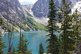 Colchuck lake, through sparse trees, with bare rock mountains behind; Apline Lakes Wilderness, Enchantments area, Washington.