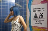 A non-binary femme person in a gender neutral bathroom