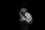 Black and white photo of a woman holding a gun. Her face is blurred and she is wearing a wedding ring. The barrel is displayed prominently.