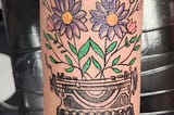 A tattoo of a classical style typewriter with wildflowers growing out the top.
