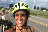 Picture of two females with sweaty foreheads wearing fluorescent yellow helmets on a cross country bike tour, smiling