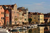 A canal in Venice lined by tall houses on the street and boats in the water