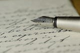 Stock photo of a white paper filled with words in cursive writing using an ink pen with one third of the pen lying on the paper