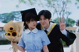 Sang Zhi holding a sunflower bouquet looking at Duan Jiaxu holding up a peace sign to click a photo together at his Graduation ceremony