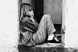 Lonely girl sitting on a doorway, face buried in her palms