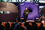 Pete standing on a stage in front of a giant inflatable 0