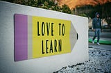 A sign with a yellow background and black lettering that says Love to Learn