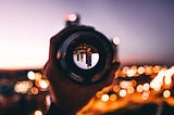 A hand holding a glass focusing on an inverted view of skyscrappers at dusk