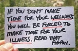 Handwritten card against out of focus grass, which reads: “If you don’t make time for your wellness you will be forced to make time for your illness. Read that again.”