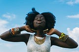 Black woman smiling with eyes closed and head pointed toward the blue sky