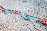 interlinked chain of alternating red and blue paperclips; the middle paperclip is broken