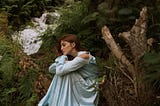 Woman in blue dress sitting on tree trunk lost in deep thoughts