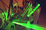 A very techy-looking device replete with several green lasers shooting in various directions in a dark laboratory.