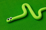 Green playdough snake complete with funny eyes and smile, on a green background.