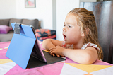 A young girl sitting at a counter, talking into an iPad.