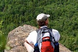 W Michael Donovan sits cross-legged on a rock outcropping while on a hike and stares out at the forest below.