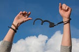Low section of man’s arms against sky breaking free of handcuffs