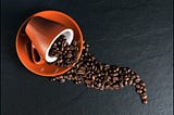 A rustic orange saucer and coffee mug. The mug is flipped over with coffee beans pouring out: Spilling the beans.