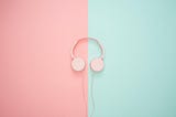 Pink headphones on a pastel background. Background is split in half vertically, left is pink, right is green