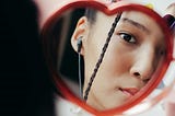 Teenage girl looking at herself in a heart shaped mirror. She has a single slim plait on in hair that falls across her cheek