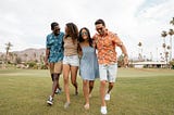 Four young men and women laughing and walking on grass in Palm Springs, California.
