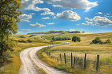 A country road winding into the distance below blue sky and clouds
