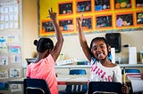 Two elementary school girls raising their hands.