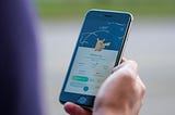 Young boy holding smartphone with Pokemon Go game displayed.