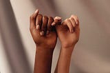 Hands of two women interlocking pinkies with one another.