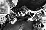 A black and white photo of a man holding a pair of gloves. 
 Carpenter with work gloves holding a drill machine.