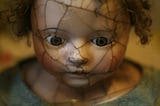 Porcelan doll face that is cracked and looking down and with the closed mouth, looking scared.