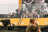 Donald Trump saluting at the 250th Army Birthday Parade with cabinet members and his wife behind him.