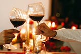 Two hands holding wine glasses on a candlelit table.