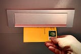 A hand grabbing a yellow envelope coming through a letterbox.