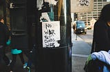 A handmade sticker reading “No war but class war” on a utility pole.