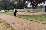 a graduate standing next to a university sign